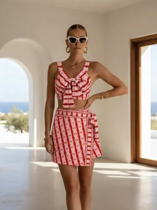 Woman in a red and white checkered outfit standing in a sunlit room with a view of the ocean.